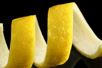 Photo of One curly lemon peel on black mirror surface, macro view