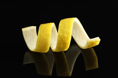 Photo of One curly lemon peel on black mirror surface, closeup