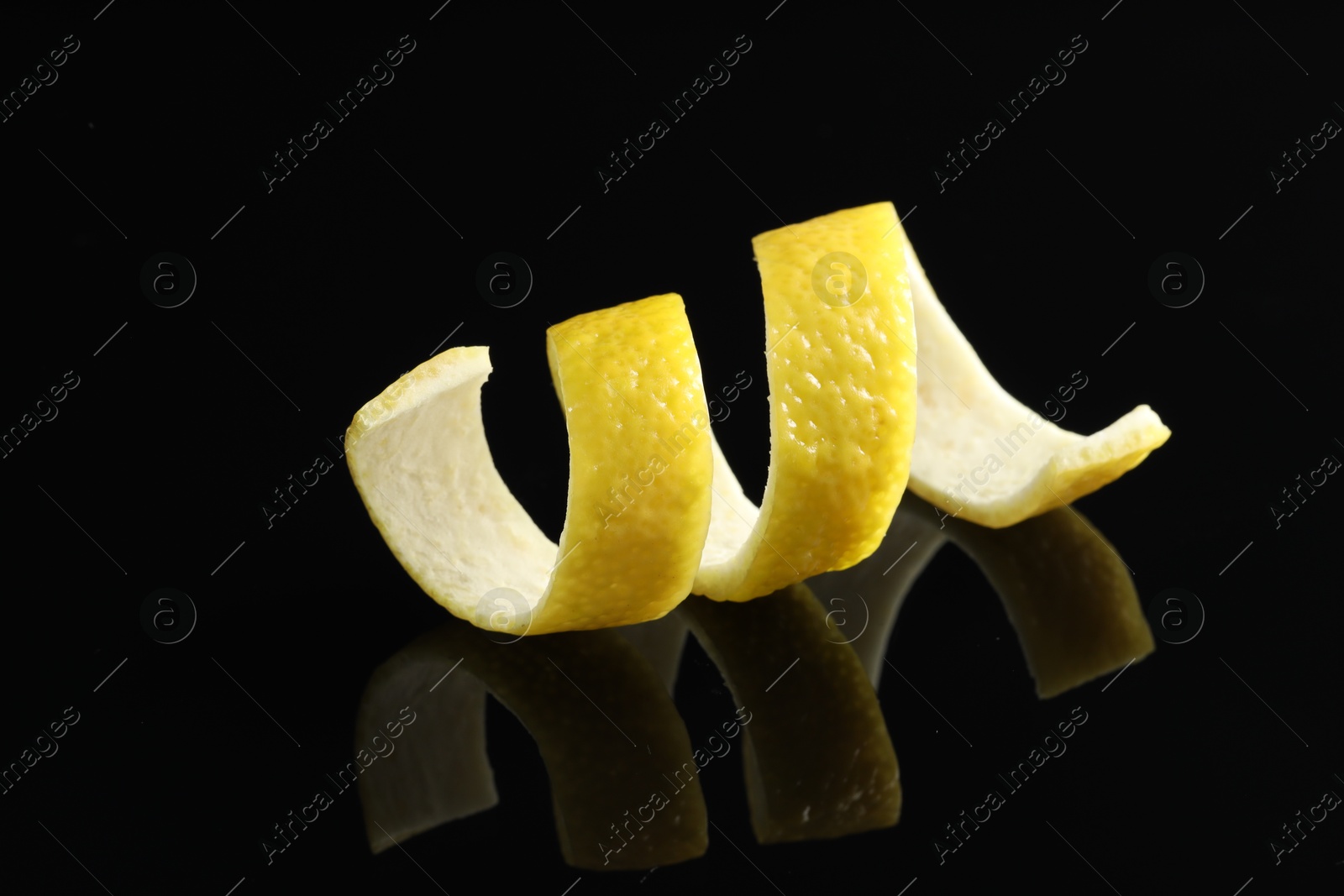 Photo of One curly lemon peel on black mirror surface, closeup