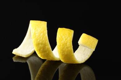 Photo of One curly lemon peel on black mirror surface, closeup