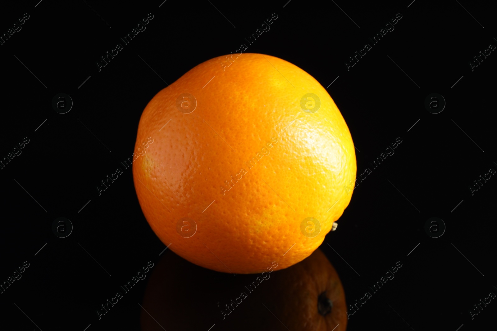 Photo of One fresh orange on black mirror surface, closeup