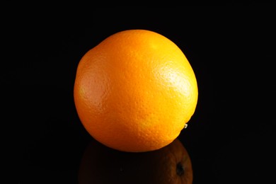 Photo of One fresh orange on black mirror surface, closeup