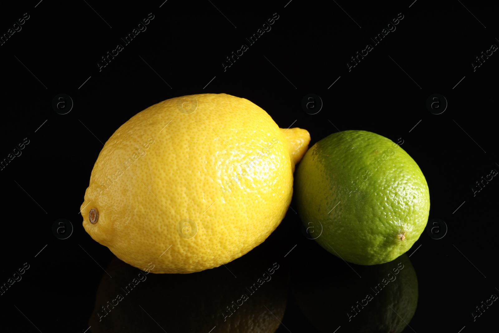 Photo of Fresh lemon and lime on black mirror surface, closeup