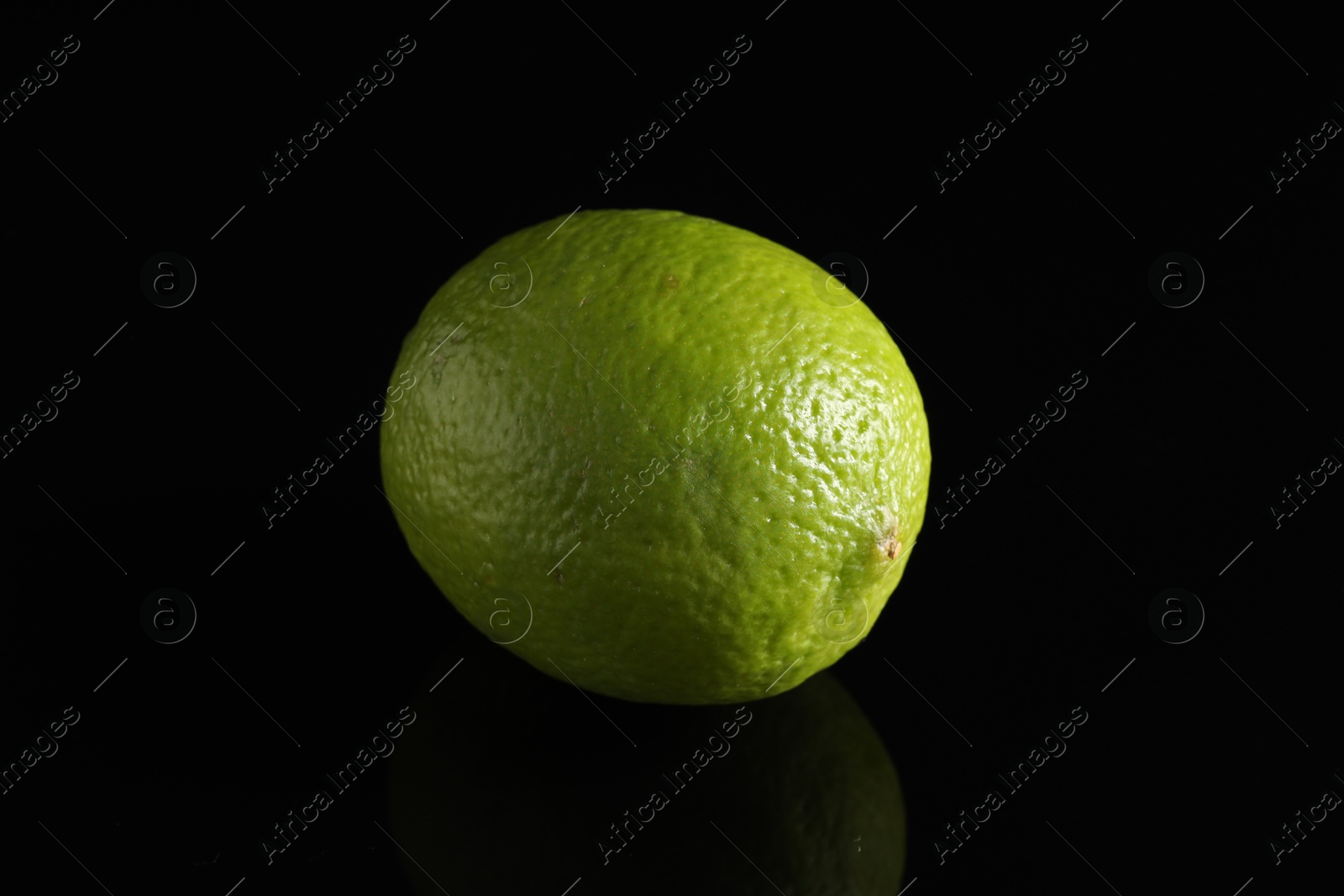 Photo of One fresh lime on black mirror surface, closeup