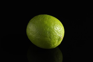 Photo of One fresh lime on black mirror surface, closeup