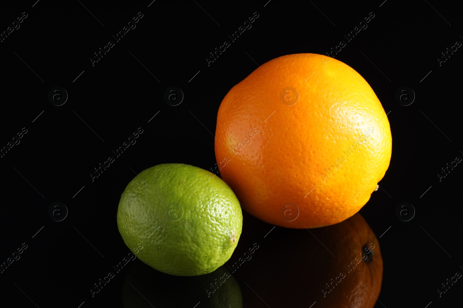 Photo of Fresh orange and lime on black mirror surface, closeup