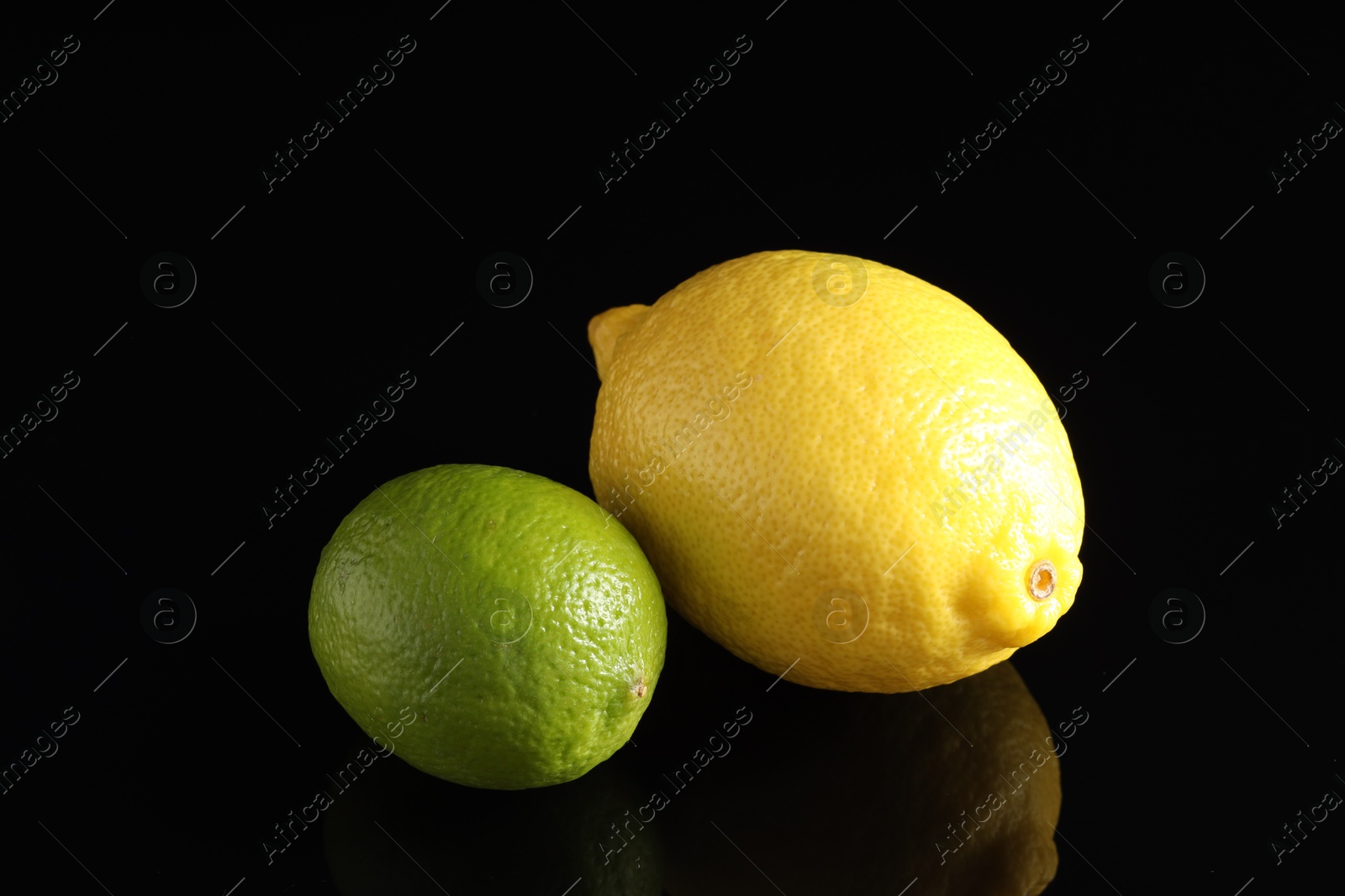 Photo of Fresh lemon and lime on black mirror surface, closeup