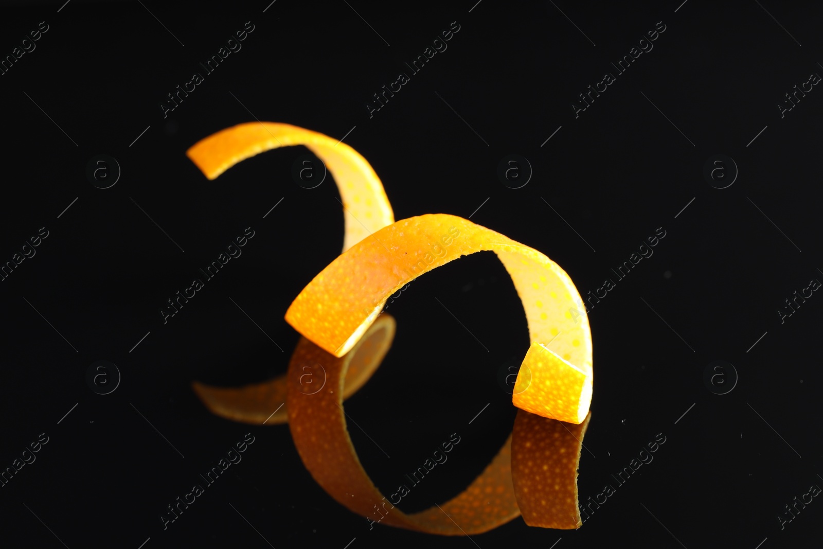 Photo of One curly orange peel on black mirror surface, closeup