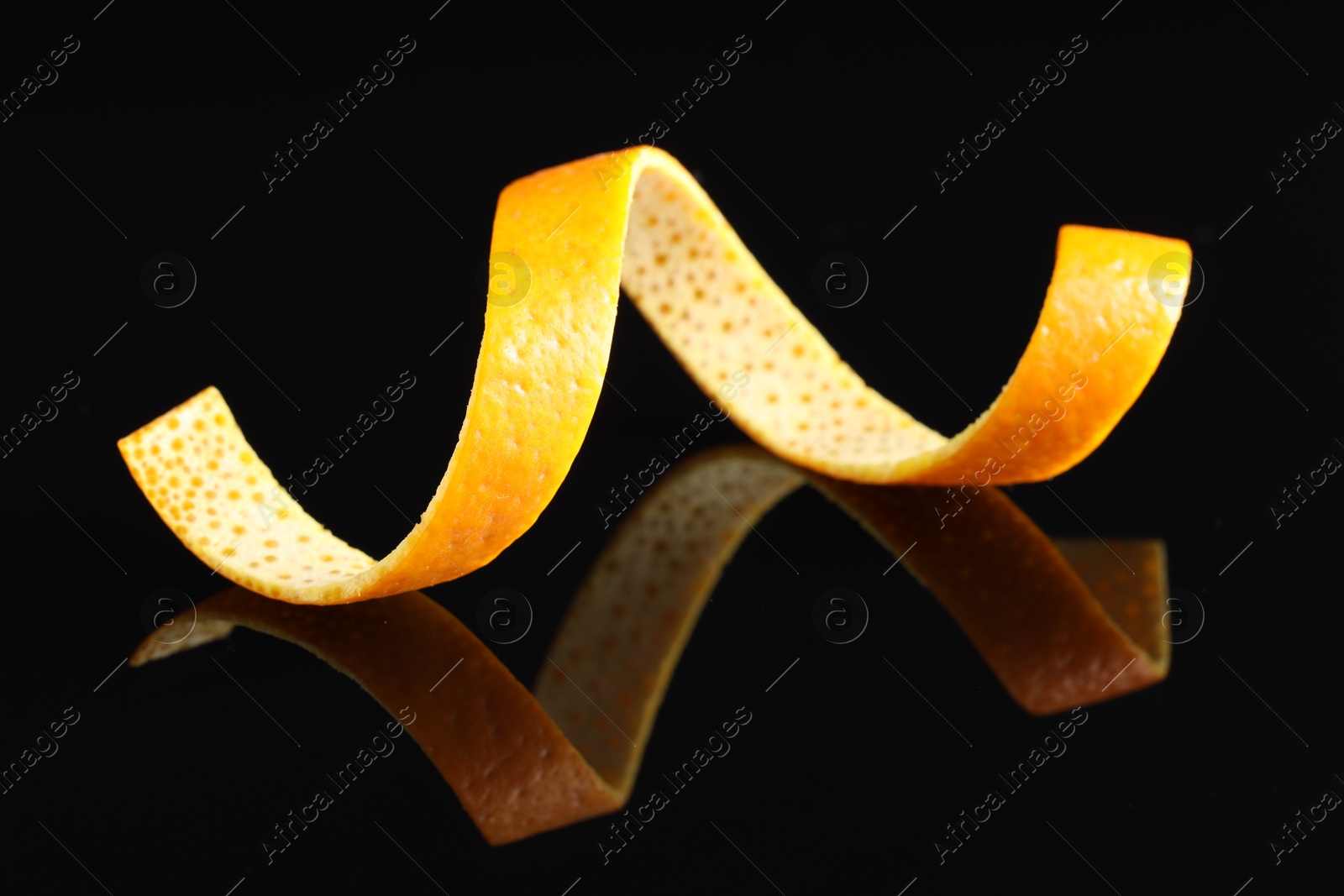 Photo of One curly orange peel on black mirror surface, closeup