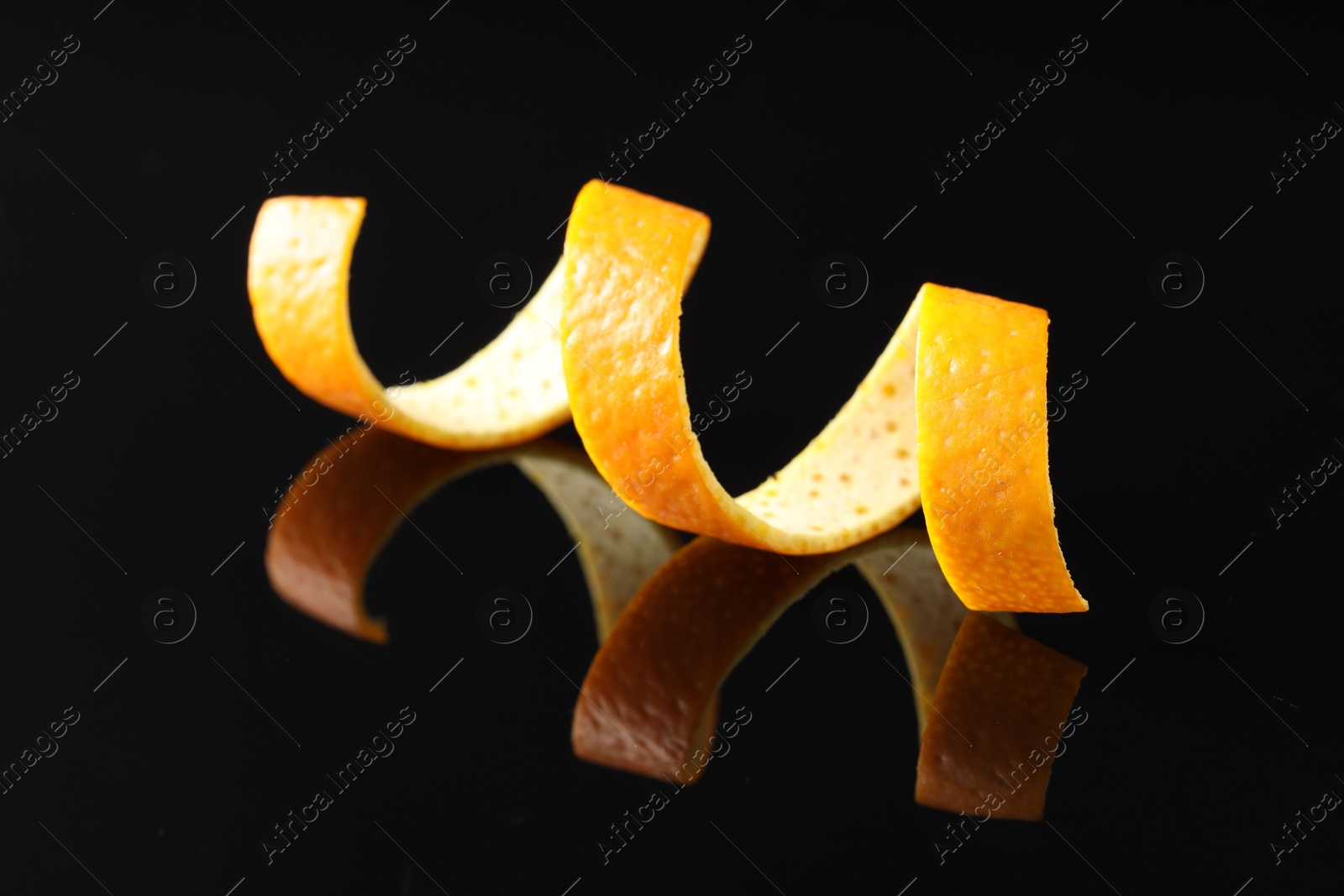 Photo of One curly orange peel on black mirror surface, closeup