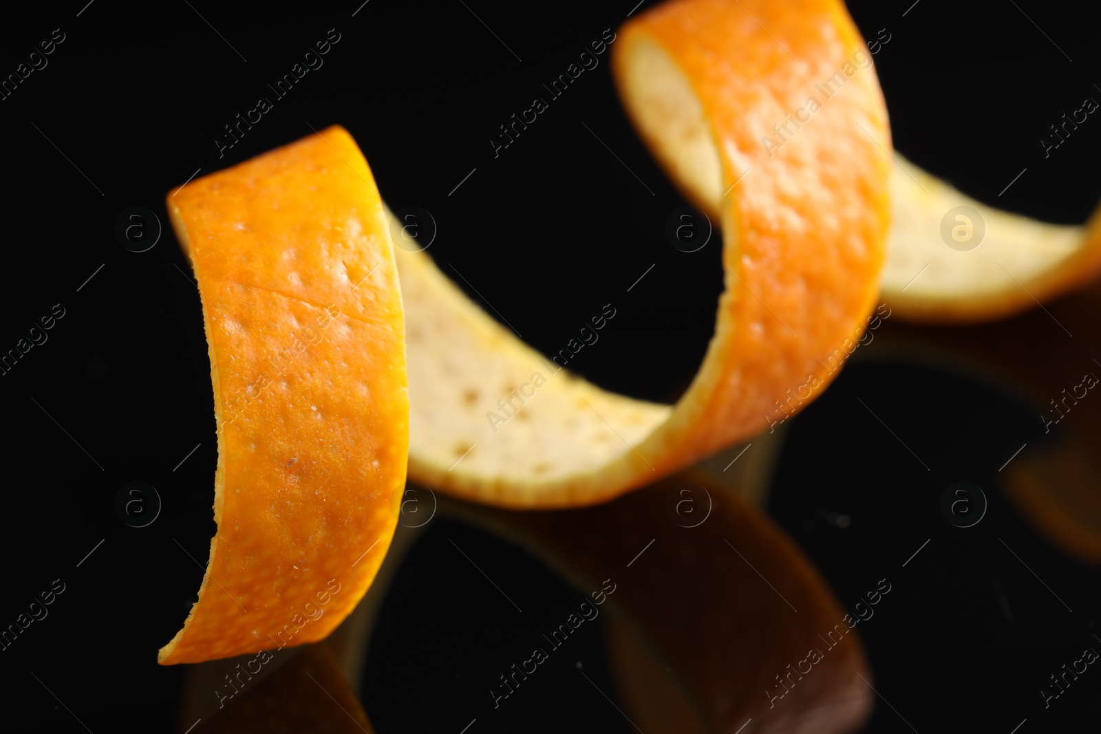 Photo of One curly orange peel on black mirror surface, macro view