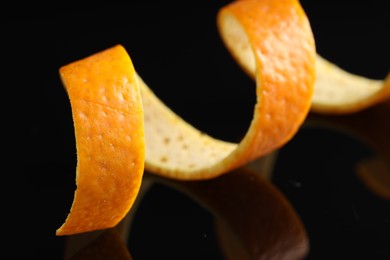 Photo of One curly orange peel on black mirror surface, macro view