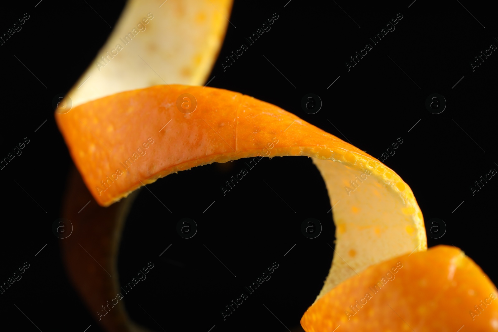 Photo of One curly orange peel on black mirror surface, macro view