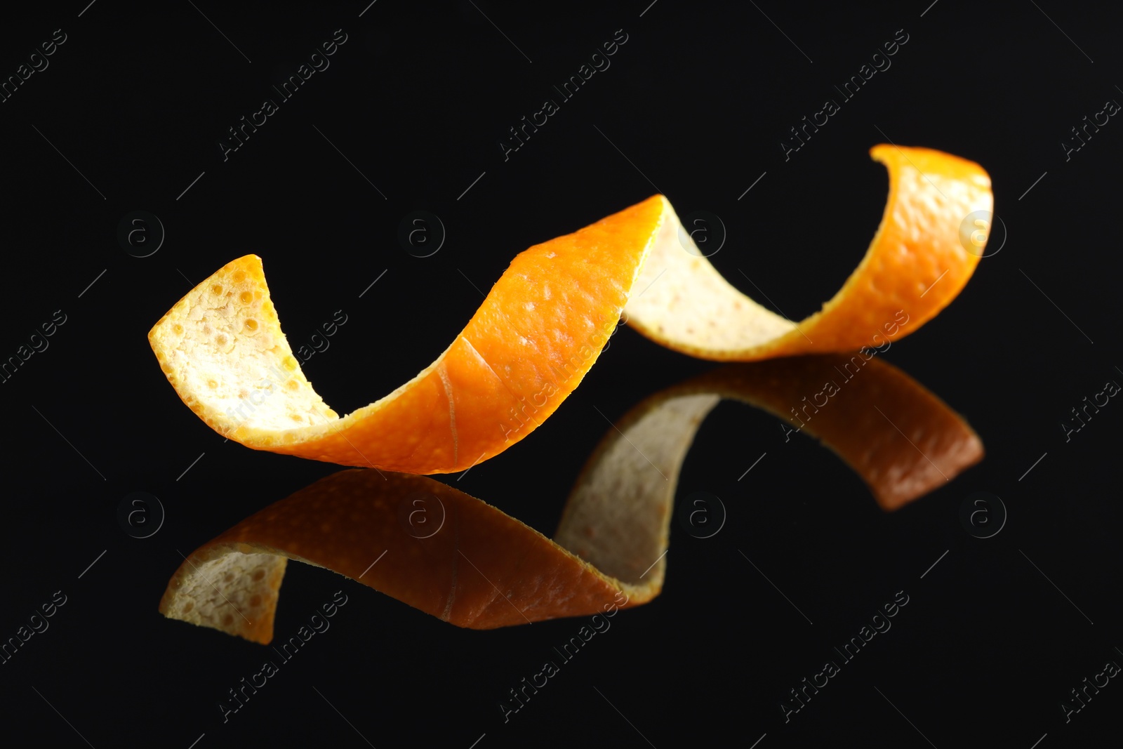 Photo of One curly orange peel on black mirror surface, closeup