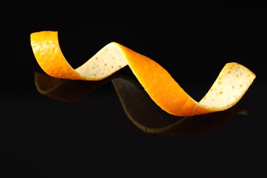 Photo of One curly orange peel on black mirror surface, closeup