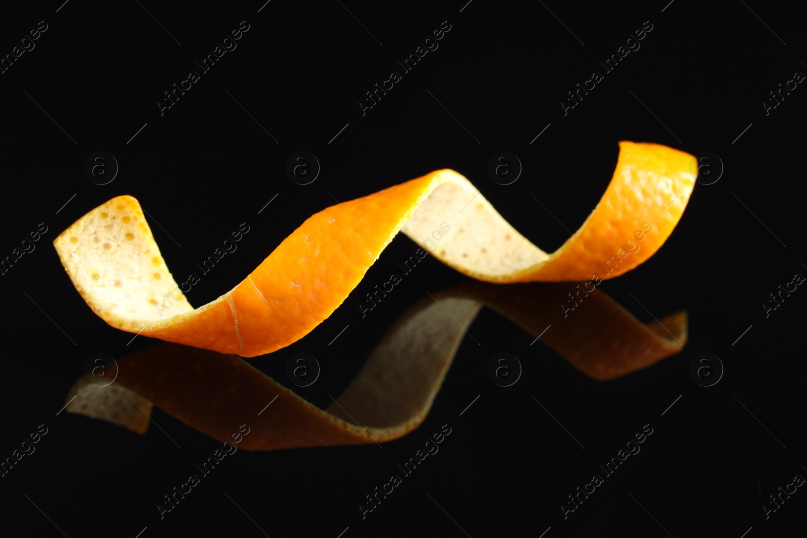 Photo of One curly orange peel on black mirror surface, closeup