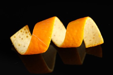 Photo of One curly orange peel on black mirror surface, closeup