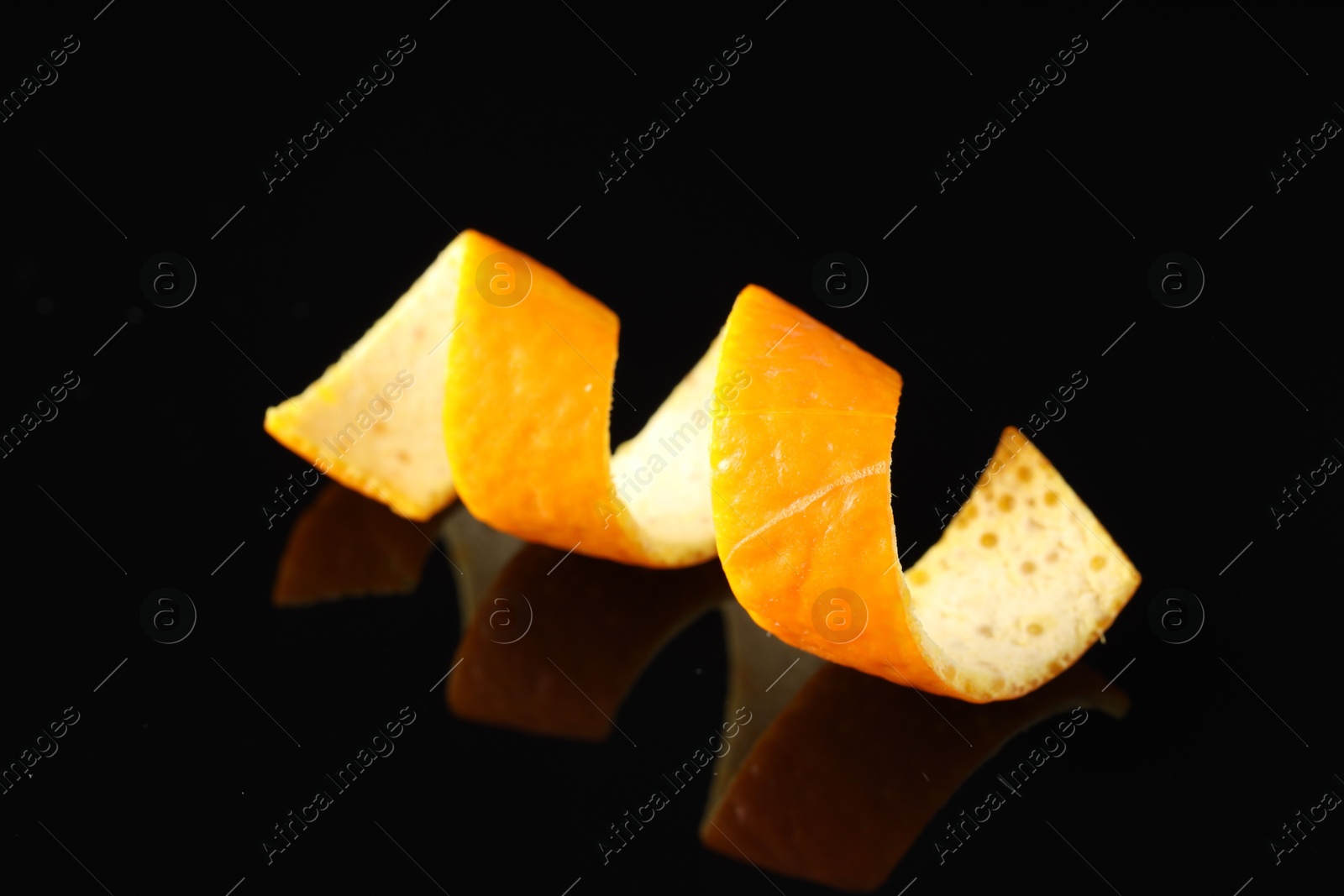 Photo of One curly orange peel on black mirror surface, closeup