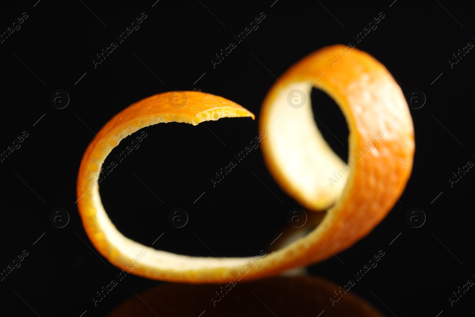 Photo of One curly orange peel on black mirror surface, closeup