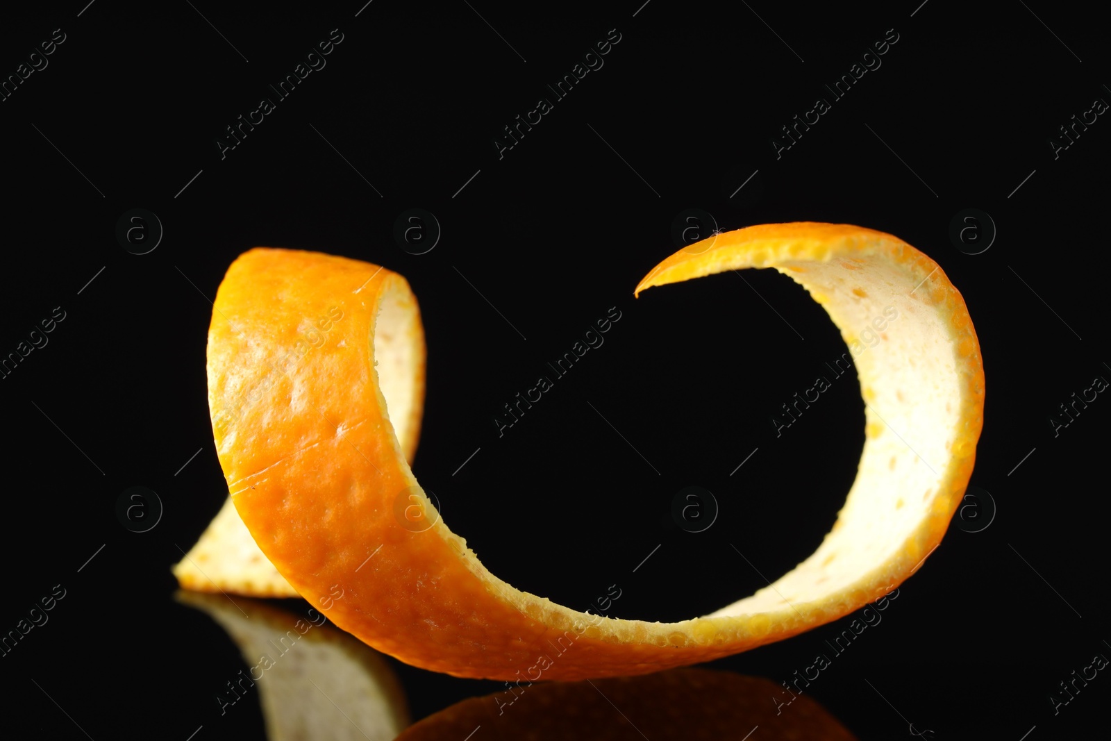 Photo of One curly orange peel on black mirror surface, closeup