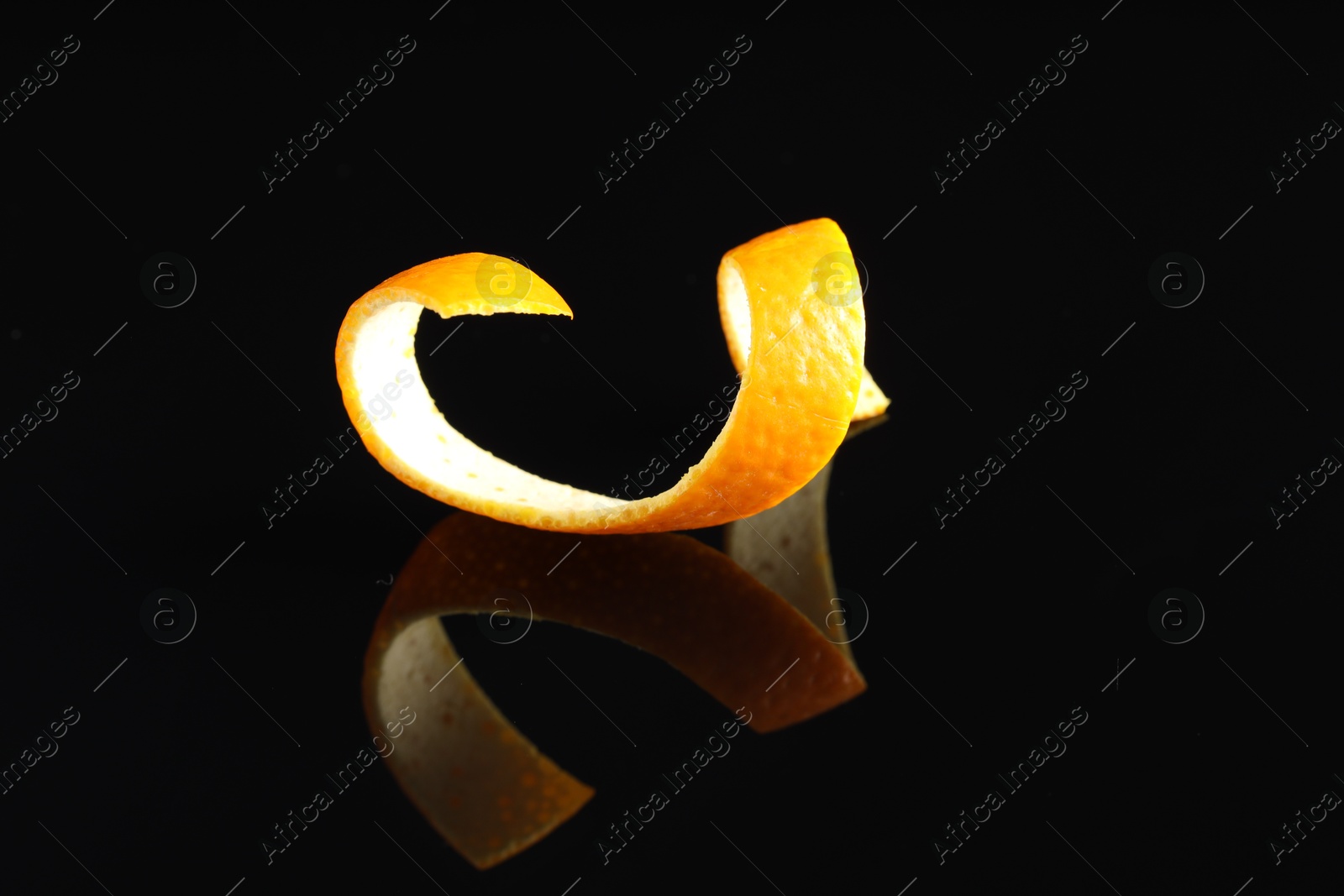 Photo of One curly orange peel on black mirror surface, closeup