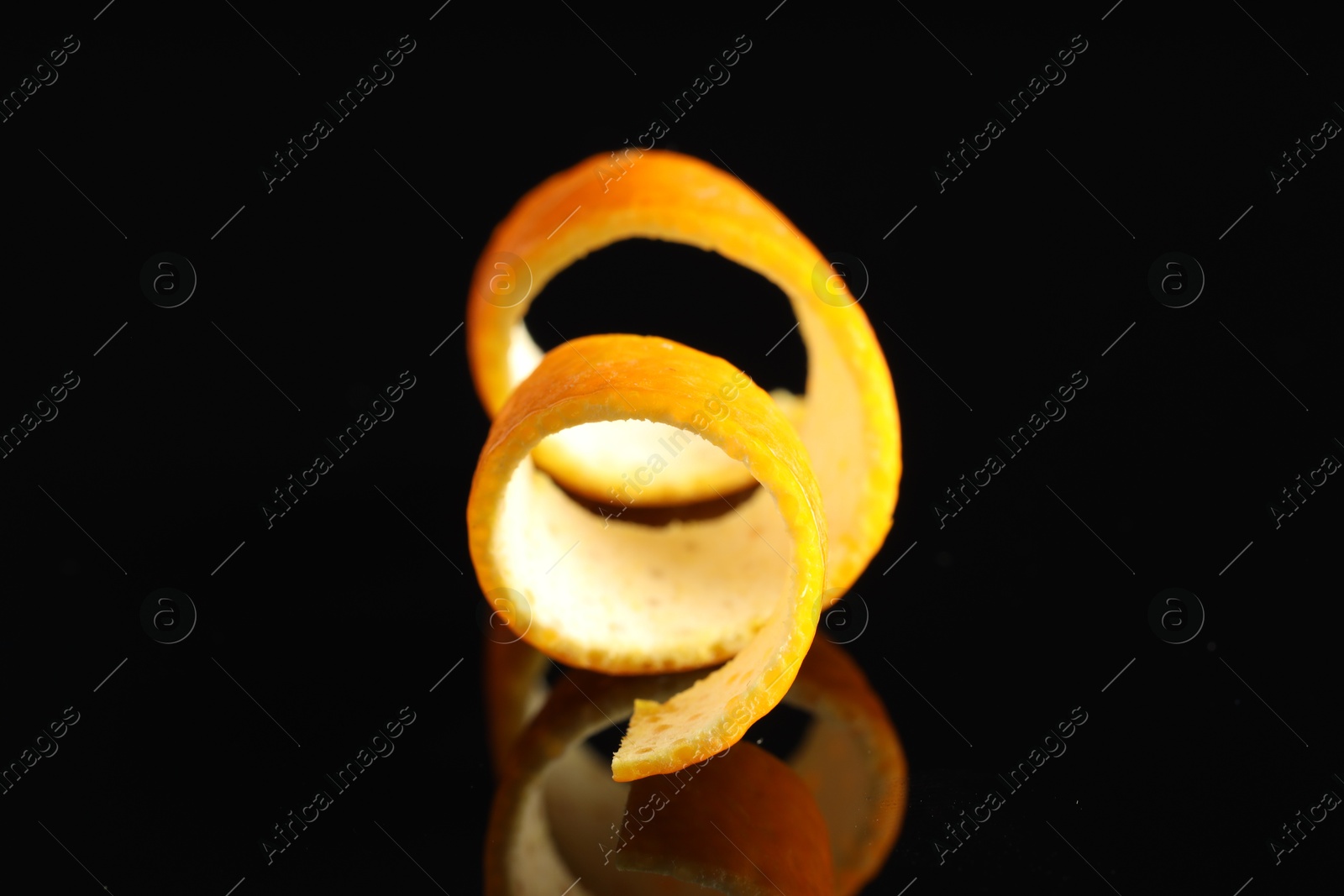 Photo of One curly orange peel on black mirror surface, closeup