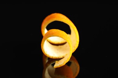 Photo of One curly orange peel on black mirror surface, closeup