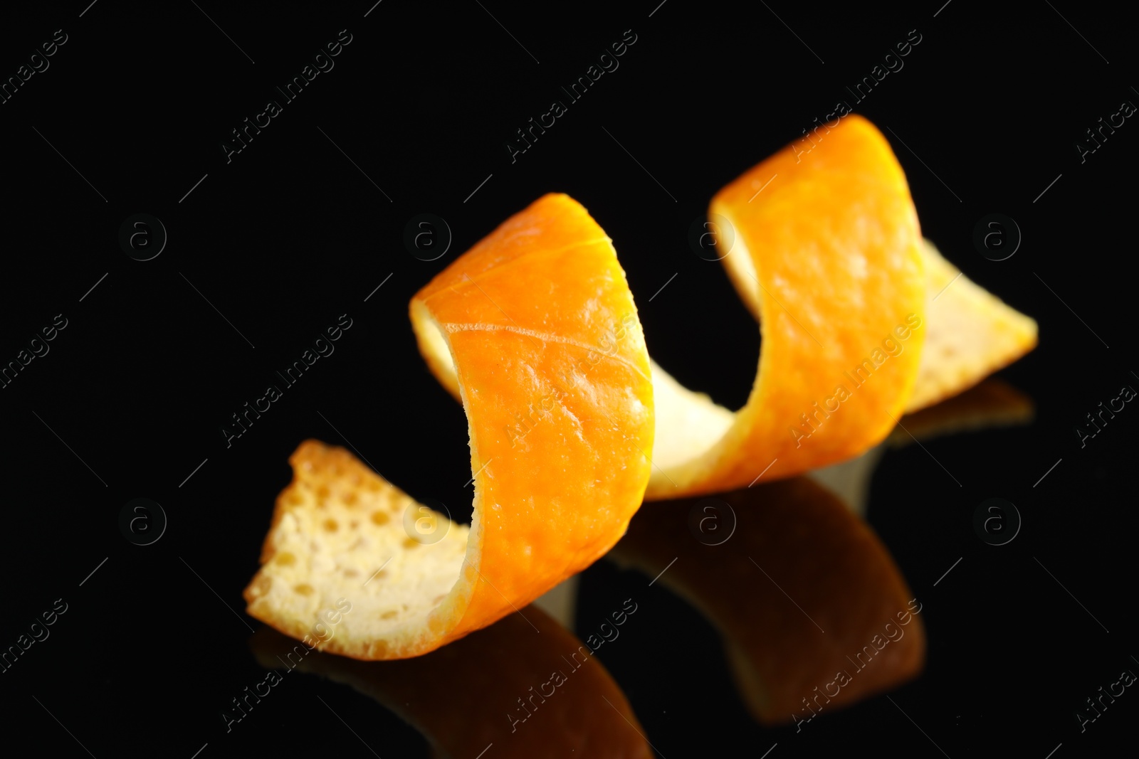 Photo of One curly orange peel on black mirror surface, closeup