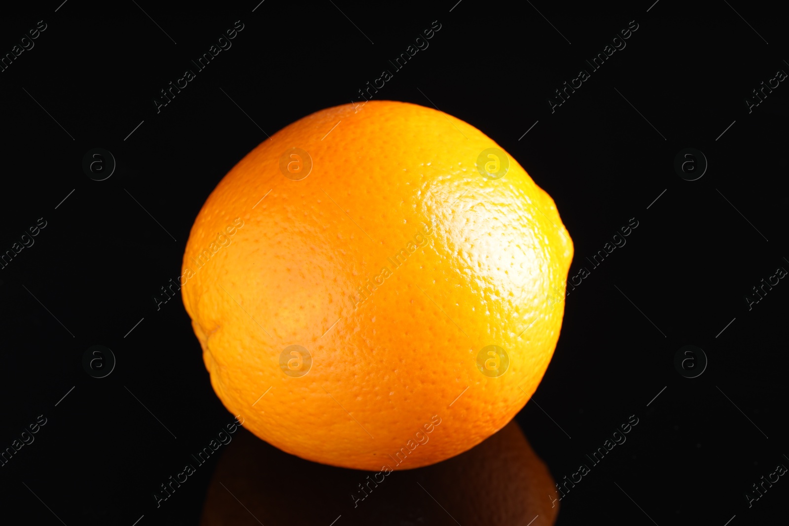 Photo of One fresh orange on black mirror surface, closeup