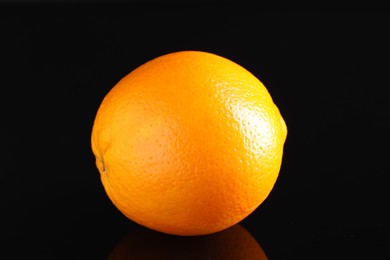 Photo of One fresh orange on black mirror surface, closeup