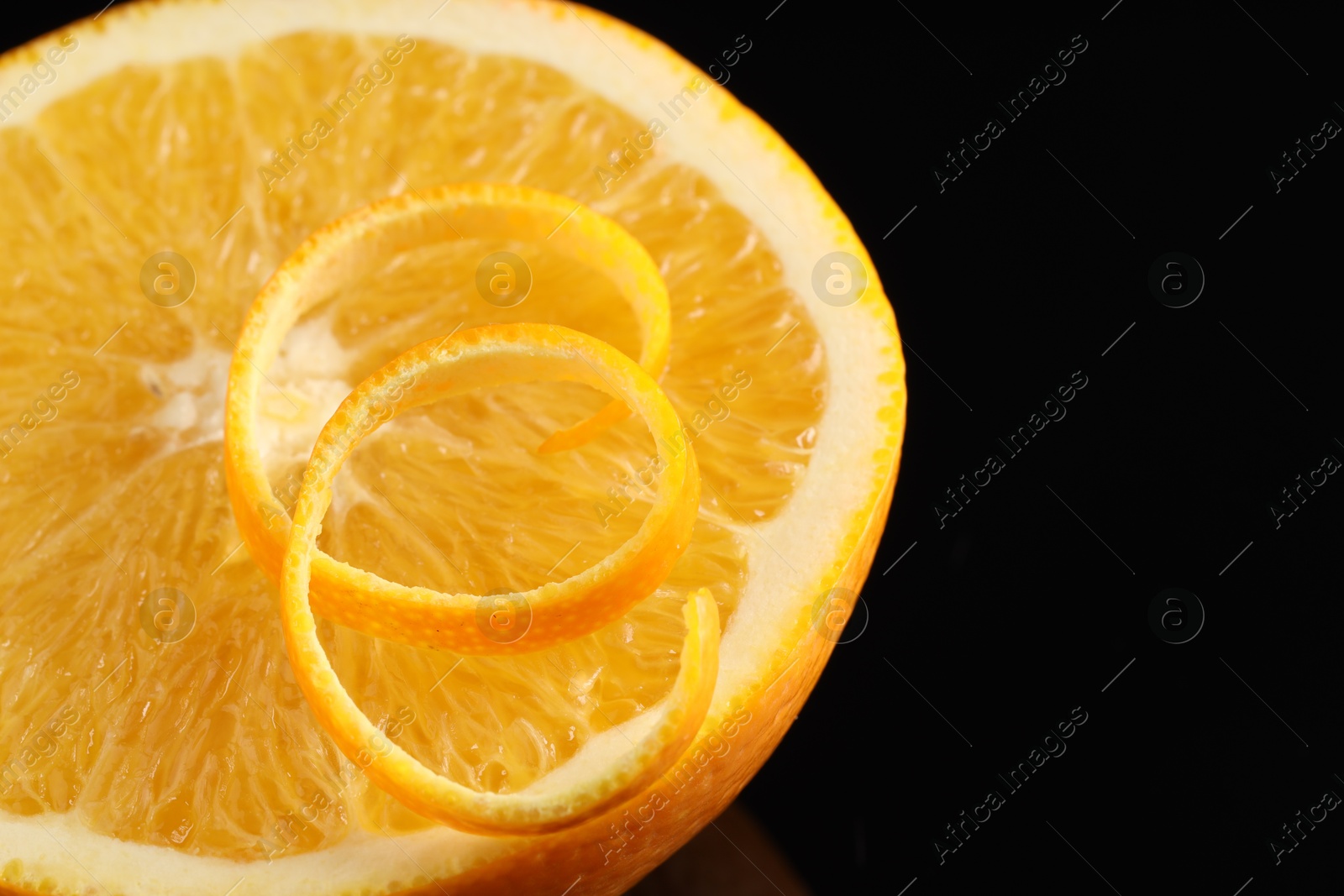 Photo of One curly orange peel and half of fruit on black background, closeup. Space for text