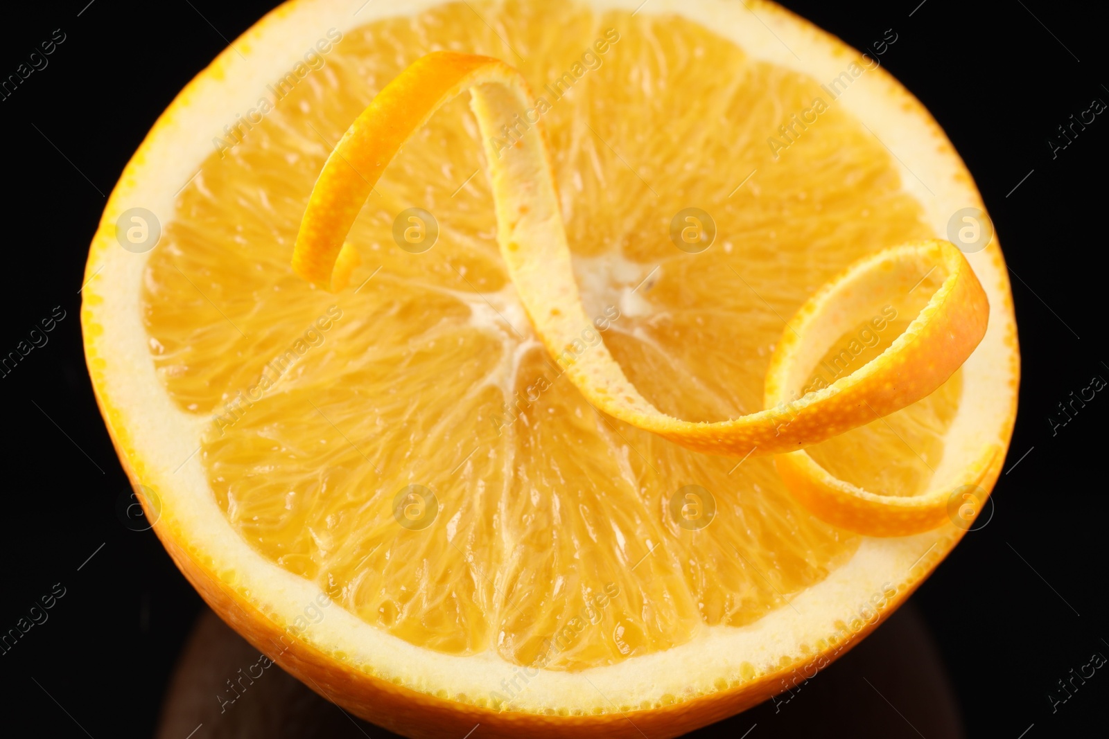 Photo of One curly orange peel and half of fruit on black background, closeup