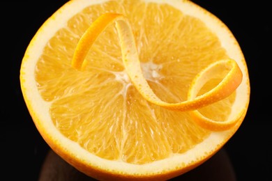 Photo of One curly orange peel and half of fruit on black background, closeup