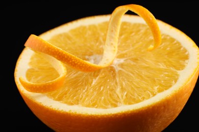 Photo of One curly orange peel and half of fruit on black background, closeup