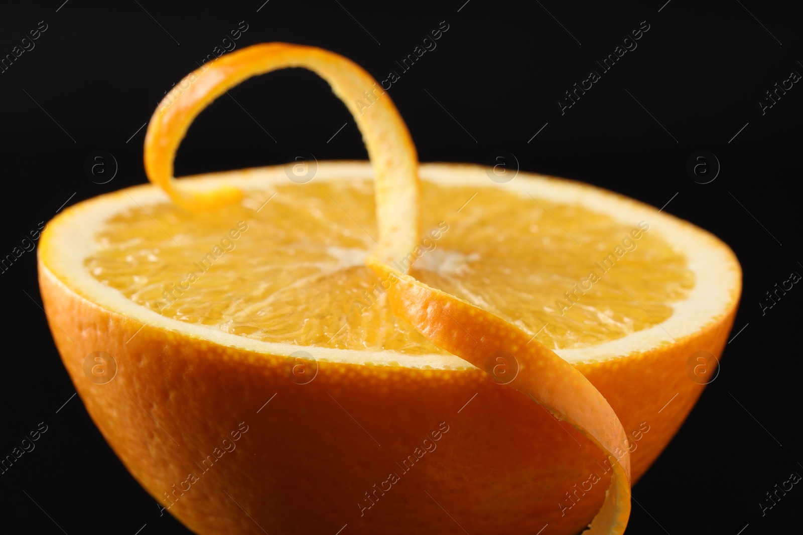 Photo of One curly orange peel and half of fruit on black background, closeup