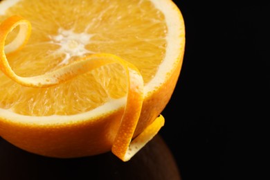 Photo of One curly orange peel and half of fruit on black mirror surface, closeup