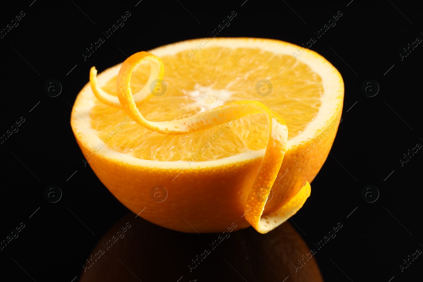 Photo of One curly orange peel and half of fruit on black mirror surface, closeup