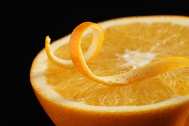 Photo of One curly orange peel and half of fruit on black background, macro view