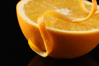 Photo of One curly orange peel and half of fruit on black mirror surface, closeup