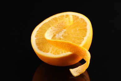 Photo of One curly orange peel and half of fruit on black mirror surface, closeup