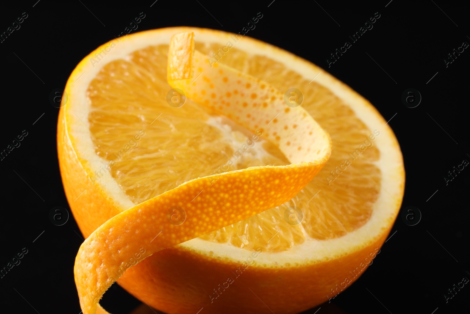 Photo of One curly orange peel and half of fruit on black background, macro view