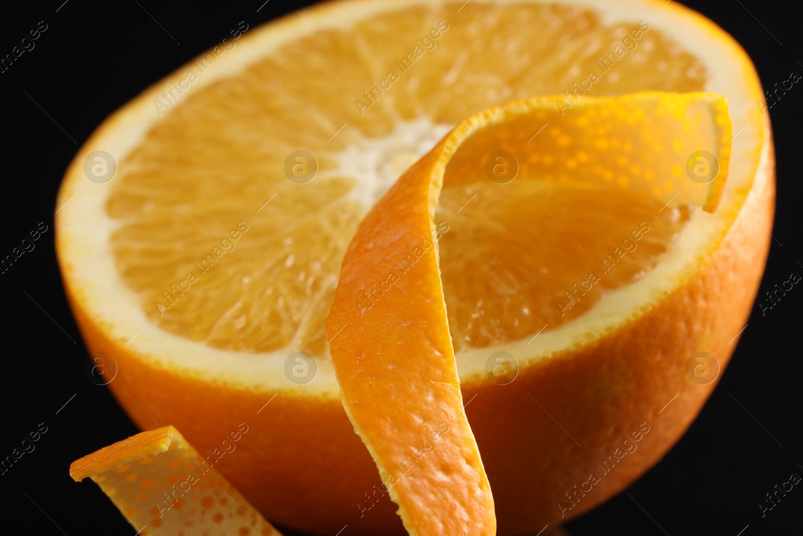 Photo of One curly orange peel and half of fruit on black background, macro view