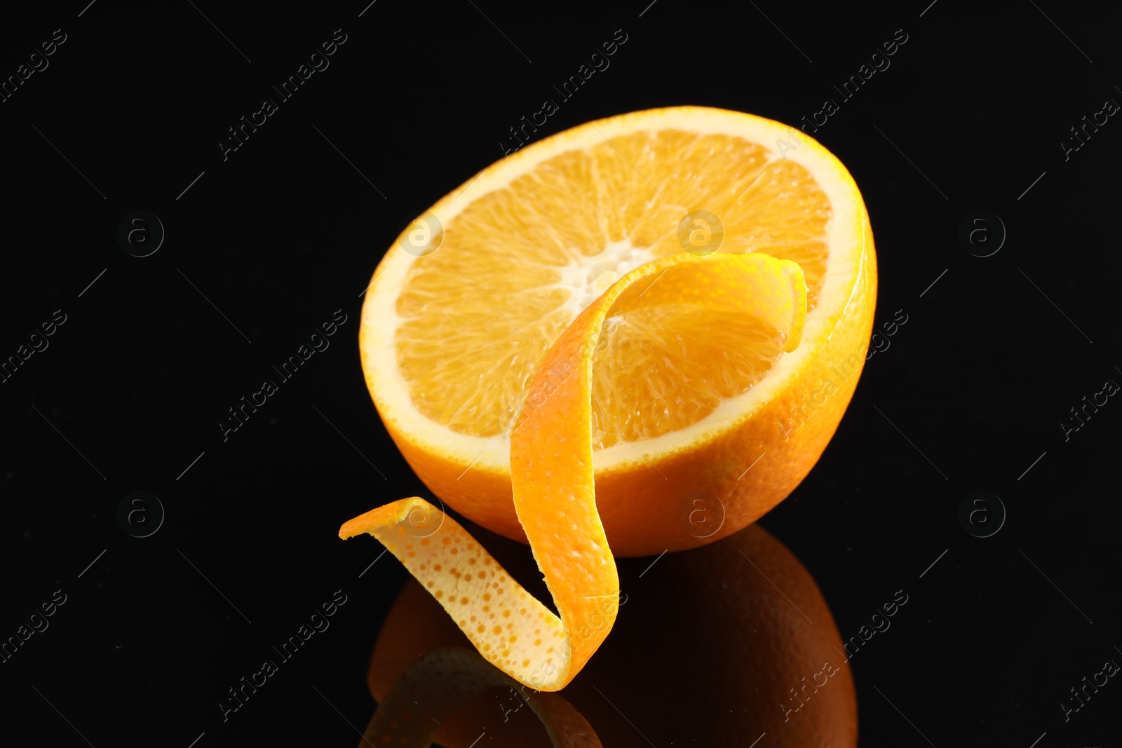 Photo of One curly orange peel and half of fruit on black mirror surface, closeup