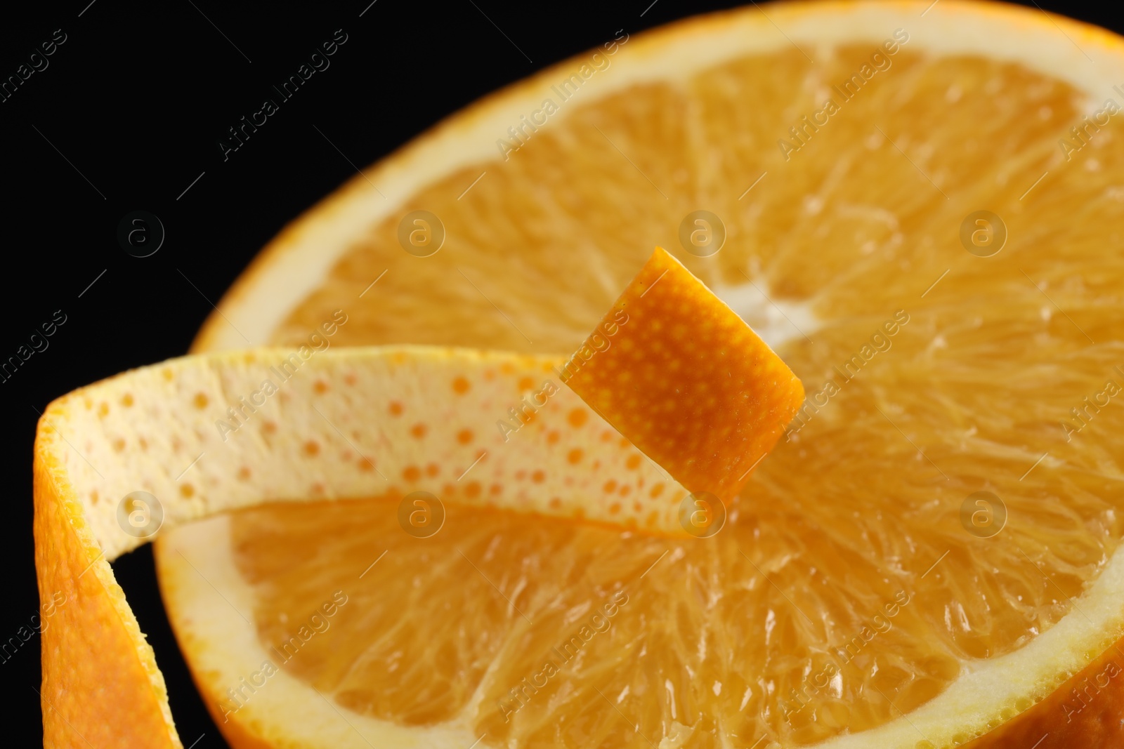 Photo of One curly orange peel and half of fruit on black background, macro view