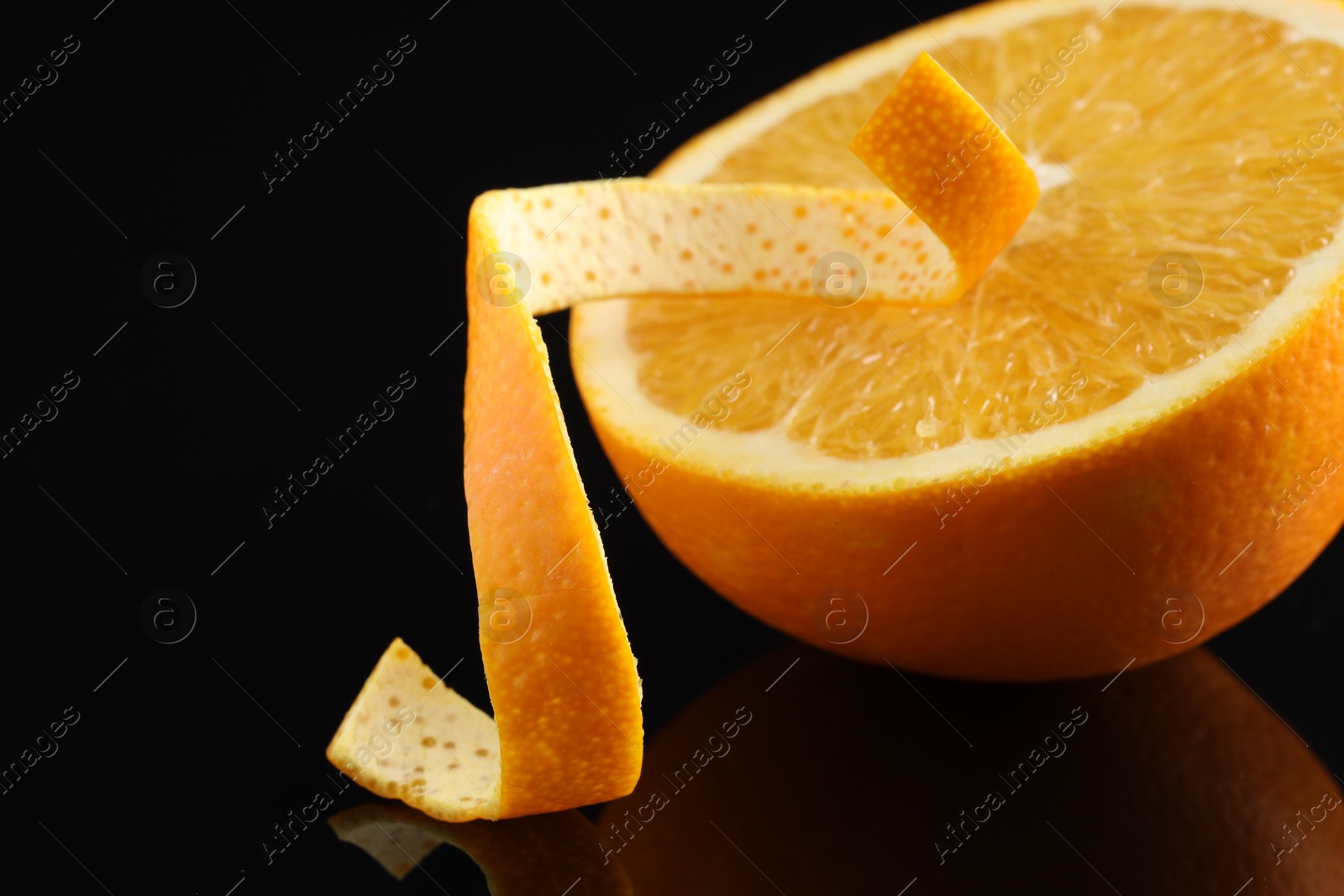 Photo of One curly orange peel and half of fruit on black mirror surface, closeup