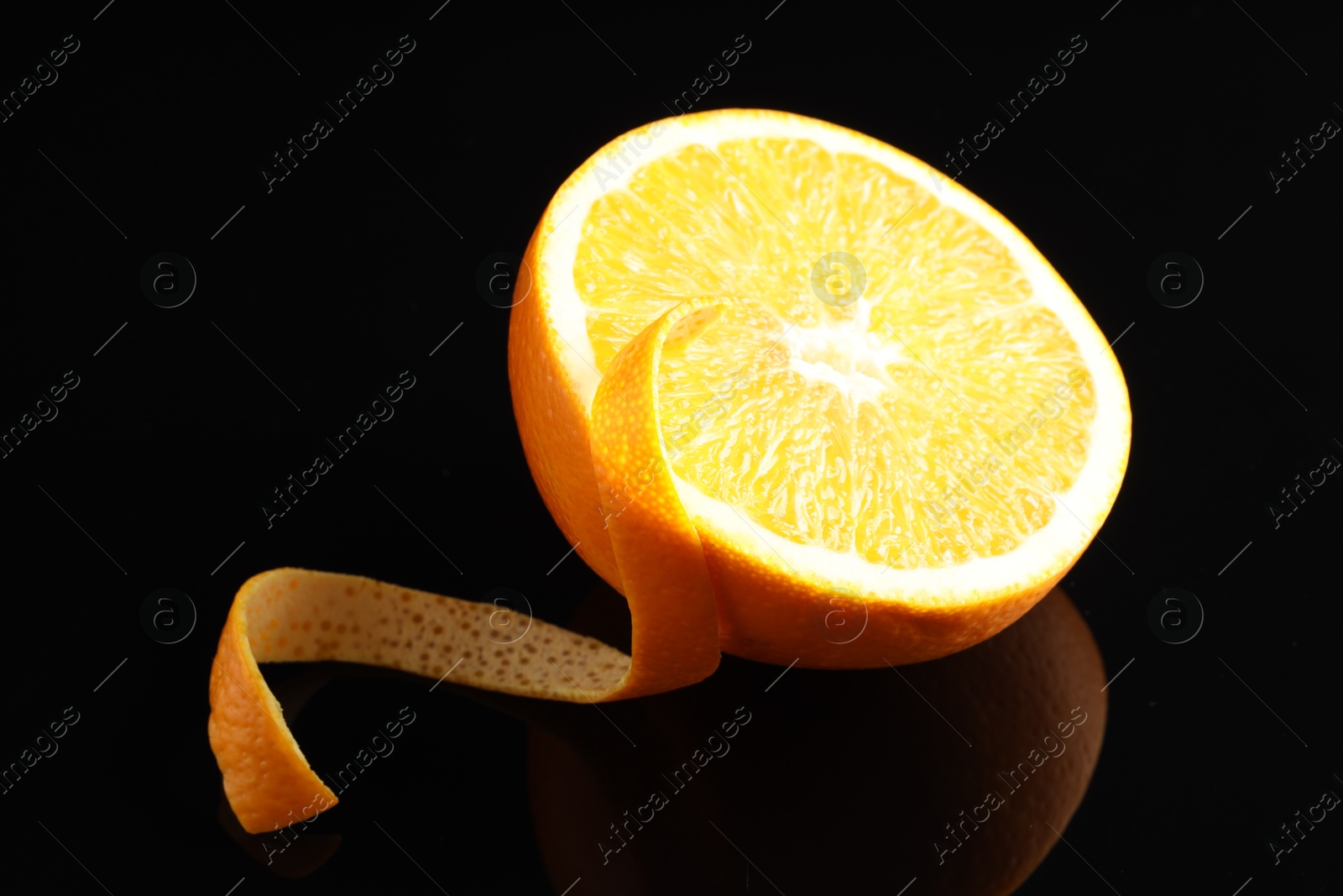 Photo of One curly orange peel and half of fruit on black mirror surface, closeup