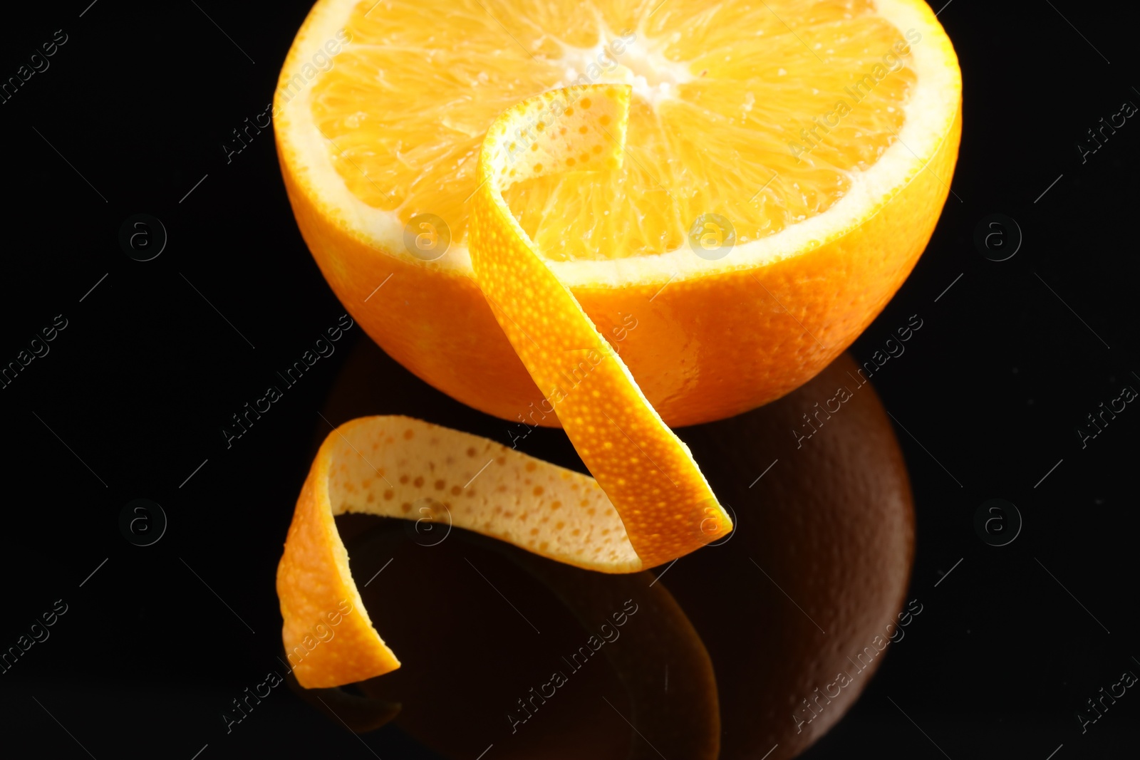 Photo of One curly orange peel and half of fruit on black mirror surface, closeup