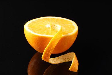 Photo of One curly orange peel and half of fruit on black mirror surface, closeup