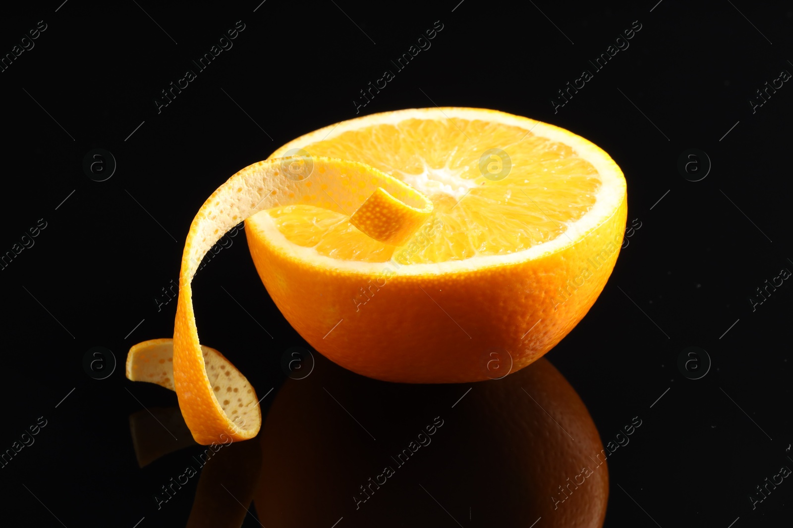 Photo of One curly orange peel and half of fruit on black mirror surface, closeup