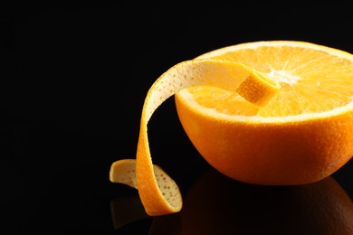 Photo of One curly orange peel and half of fruit on black mirror surface, closeup. Space for text